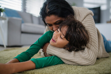 Indian mother lying on floor and having fun with her little son at home.