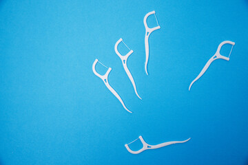 Dental flossers cleaning on blue background. Dental care concept. White toothpick and dental floss isolated. Plastic white dental toothpick with floss laid.