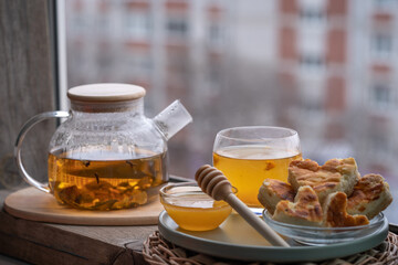 composition with a glass teapot and glass cup filled with tea and cake on the plate