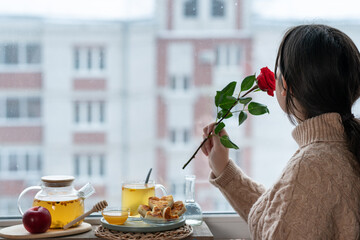 a girl sniffs a rose next to a glass teapot with tea and a cake in the form of hearts
