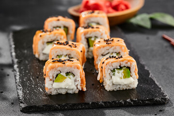 Maki sushi on dark slate. Hot philadelphia maki with baked salmon. Sushi roll with grilled salmon, cream cheese and avocado. Style concept japanese menu with black background, leaves and hard shadow.