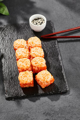 Baked Maki sushi on dark slate. Hot california maki with tobiko. Sushi roll with masago caviar, cheese topped baked oven. Style concept japanese menu with black background, leaves and hard shadow.