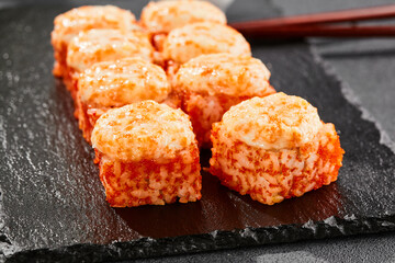 Baked Maki sushi on dark slate. Hot california maki with tobiko. Sushi roll with masago caviar, cheese topped baked oven. Style concept japanese menu with black background, leaves and hard shadow.