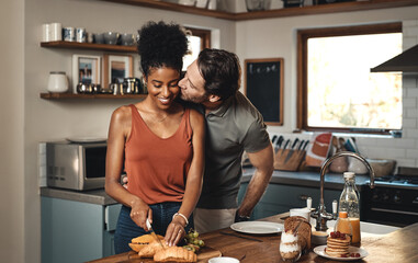Theres no way Im skipping breakfast with you. Shot of a man kissing his wife while she prepares breakfast in the kitchen at home.