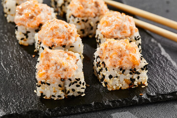 Baked Maki sushi on dark slate. Hot sushi roll with salmon and cheese. Sushi roll sesame outside, baked salmon and cheese topped. Style concept japanese menu with black background, leaves and shadow.