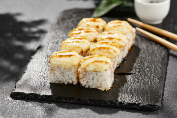 Baked Maki sushi on dark slate. Hot cheese maki with unagi sauce. Sushi roll with baked cheese and unagi sauce topped. Style concept japanese menu with black background, leaves and hard shadow.