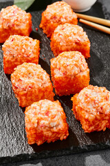 Baked Maki sushi on dark slate. Hot california maki with crab. Sushi roll with masago outside, baked cheese and crab topped. Style concept japanese menu with black background, leaves and hard shadow.