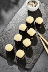 Baked Maki sushi on dark slate. Hot cheese hosomaki roll. Simple sushi roll with cheese, baked cheese topped. Style concept japanese menu with black background, leaves and hard shadow.