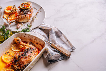 roasted fried turkey duck thighs, rubbed with spices and salt, on a baking sheet, with oranges, lemons, garlic, rosemary, thyme and olive oil. the concept of a healthy and tasty dinner for two.