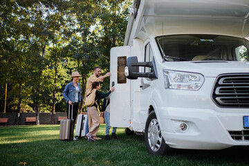 Young family with suitcases entering caravan outdoors at park. - obrazy, fototapety, plakaty