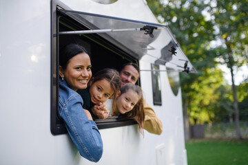 Happy young family with two children looking out of caravan window.