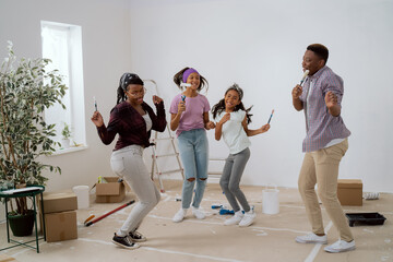 Crazy happy family painting the walls with white paint with brushes, they dance in the middle of the room, singing, parents play with children, the house prepared for renovation