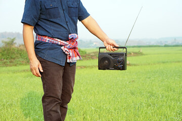 Farmer holds FM-AM radio receiver at paddy field. Concept : Happy working along with music. Country...