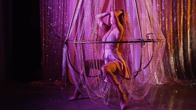Sexy young woman in silver dress with rhinestones posing inside large decorative chandelier made of crystal beads