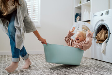 Mom is playing with daughter who is sitting in laundry bowl little girl wants to spend time with...