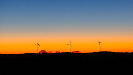 Fototapeta na wymiar Silhouettes of three wind turbines against a magnificent colored evening sky with cloudless sky in the evening
