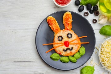 Mini easter bunny pizza on black plate with white wood background.Art food idea for kid Easter's...