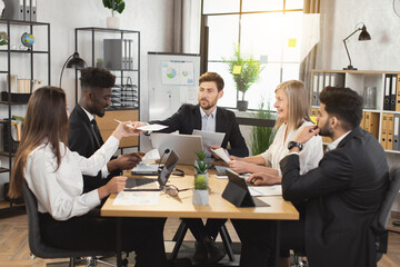 Group of five multiracial business people in formal clothes having meeting with modern gadgets and documents at boardroom. Concept of teamwork and cooperation.