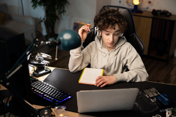 Fototapeta na wymiar Smart young boy uses laptop to learn, records useful information. distance learning, e-Education, e-Learning. Portrait of a boy doing his homework.