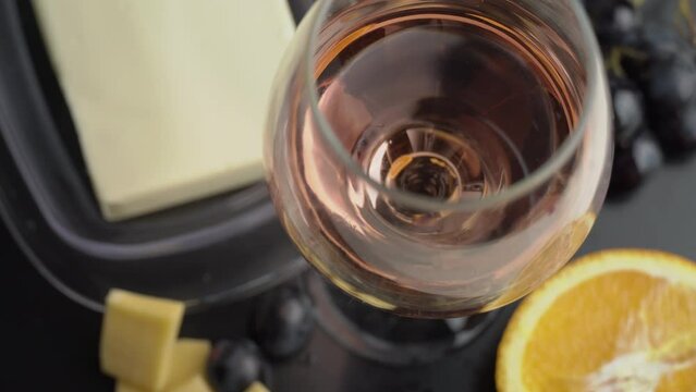 A glass of ros wine swirls with appetizers. Aesthetics of wine with cheese. Alcohol, romance, evening. Cheese, butter, red caviar, grapes, baguette, orange. View from above.