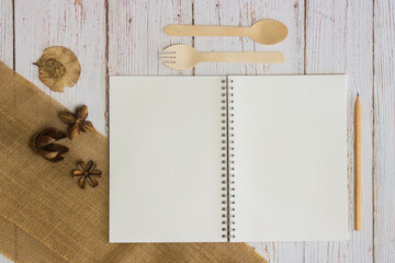 recipe book with wooden spoon and fork over the wooden background. 