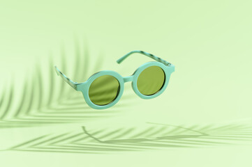 Levitating retro sunglasses over pastel green background, with shadows palm leaves. Creative summer minimal scene. Vacation, holidays, and party concept.