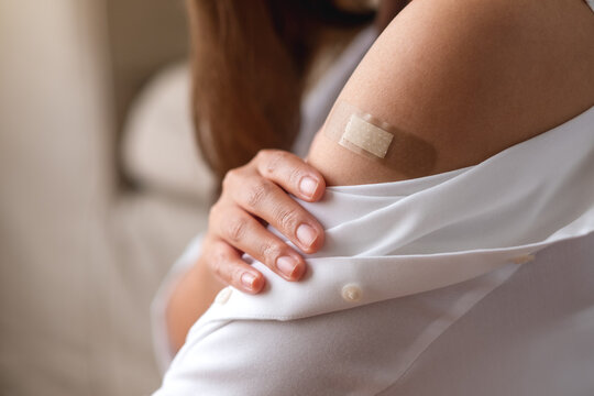 Closeup image of a young woman with adhesive bandage, medical plaster, band aid on her shoulder for vaccination concept