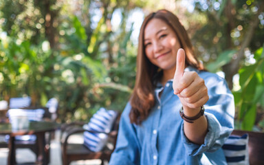 Blurred of a young woman making and showing thumbs up hand sign - obrazy, fototapety, plakaty
