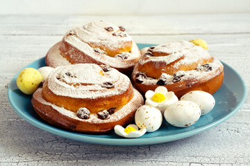 Easter decor with sugar flowers and chocolate eggs with round spiral buns on a blue plate