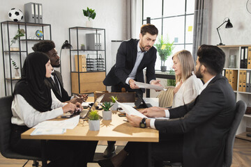 Group of focused business partners gathering together at boardroom for negotiation. Five competent bankers discussing company situation on meeting.