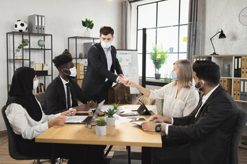 Multiracial business people in face masks greeting with fists during conference at office. Preventive measures during pandemic. Teamwork concept.