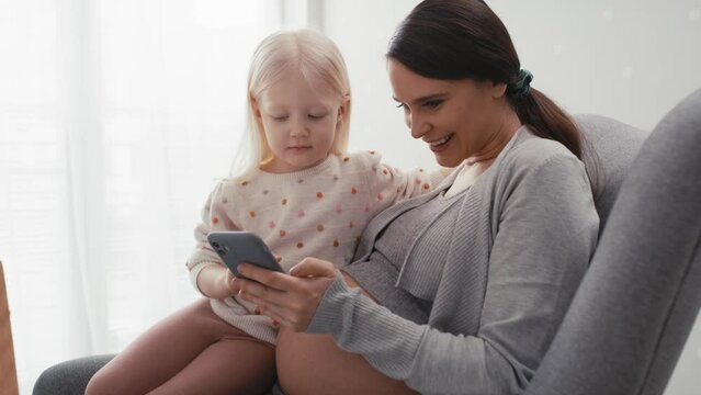 Caucasian woman in advanced pregnancy and her elementary aged daughter using mobile phone at home