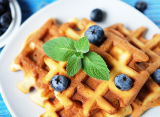 Homemade Belgian waffles served with fresh berries on white plate over wooden background, close up.