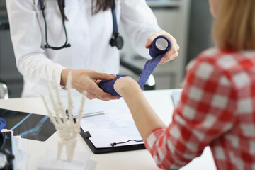 A doctor in clinic bandages woman's wrist with an elastic band