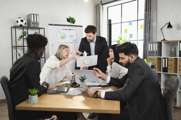 Diverse group of business partners discussing development of common project during meeting at boardroom. Colleagues doing paperwork and using modern technology.