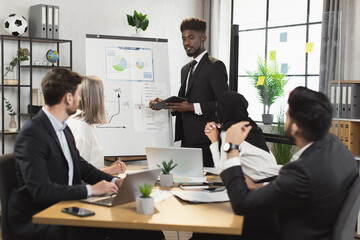 African american man in suit explaining working issues at briefing with multiracial colleagues at office. Company workers gathering at boardroom for intense negotiation.