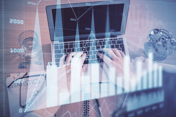 Double exposure of man's hands typing over laptop keyboard and forex chart hologram drawing. Top...