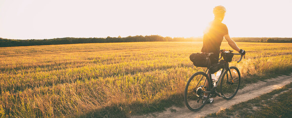 Bike traveler riding through the field at sunset on bicycle with bags