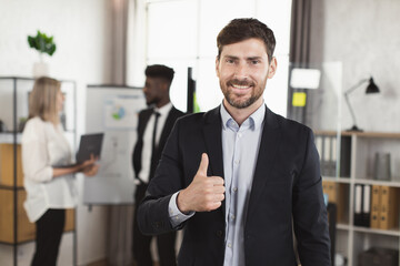 Portrait of positive caucasian businessman in suit looking and smiling on camera at boardroom while...