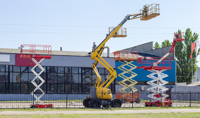 Different scissor and articulated boom wheeled lifts against industrial building