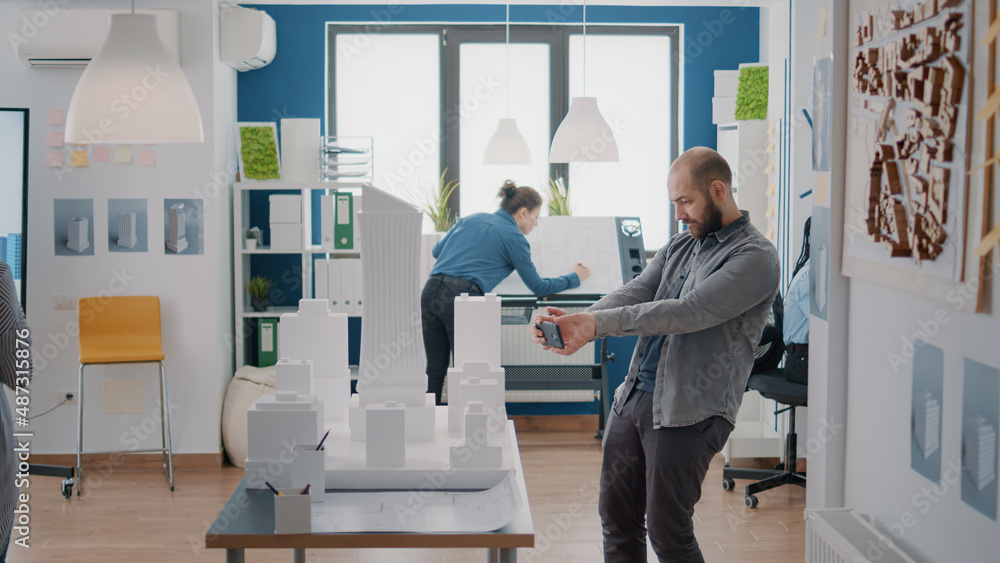 Poster man using smartphone to design building model and construction layout with maquette in office. engin