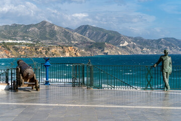 View from Balcony of Europe in Nerja, Malaga. Statue of King Alfonso XII. Old wooden Cannon. Sierra Nevada mountains in background  © alexemarcel