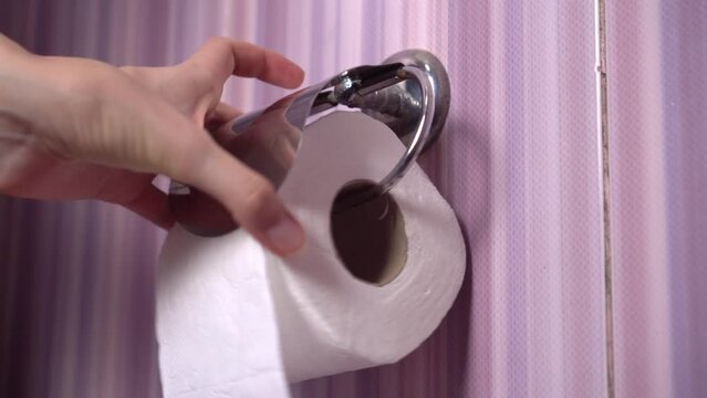 Close-up of female hands that place a roll of toilet paper in a holder in the toilet. It's rusty and old. The concept of personal hygiene.