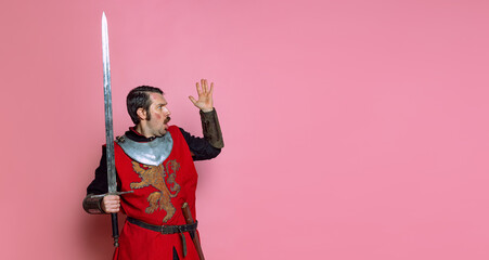 Portrait of shocked medieval warrior or knight wearing wearing armor clothing holding big sword...