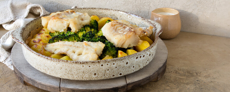 dish with baked potatoes, broccoli and codfish on the table