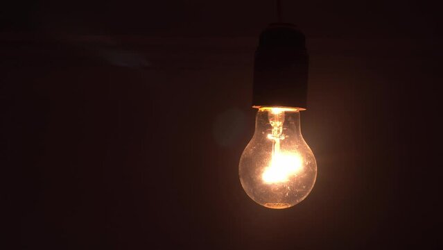 A lamp with a tungsten bulb assembly slowly turns on and off on a black background, a close-up shot of an old retro-vintage light bulb brightening the light. A comfortable cozy concept.