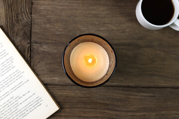 the burning luxury aromatic scented candle glass on the wooden table with a cup of coffee and book in the living room to creat relax ambient after hard working all day