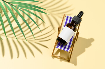 Brown dropper glass bottle lies on lounge chair under palm leaf shade on pastel yellow background. Skincare during sunbathing concept. Organic mineral cosmetic product. Mock up, showcase