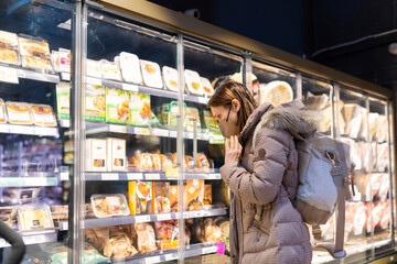 woman with a face mask doing the shopping in the supermarket in the precooked and packaged dishes area. processed food