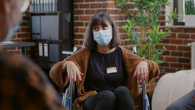 Close up of woman with face mask sitting in wheelchair at aa group meeting. Person with disability having conversation about mental health problems and alcohol addiction during pandemic